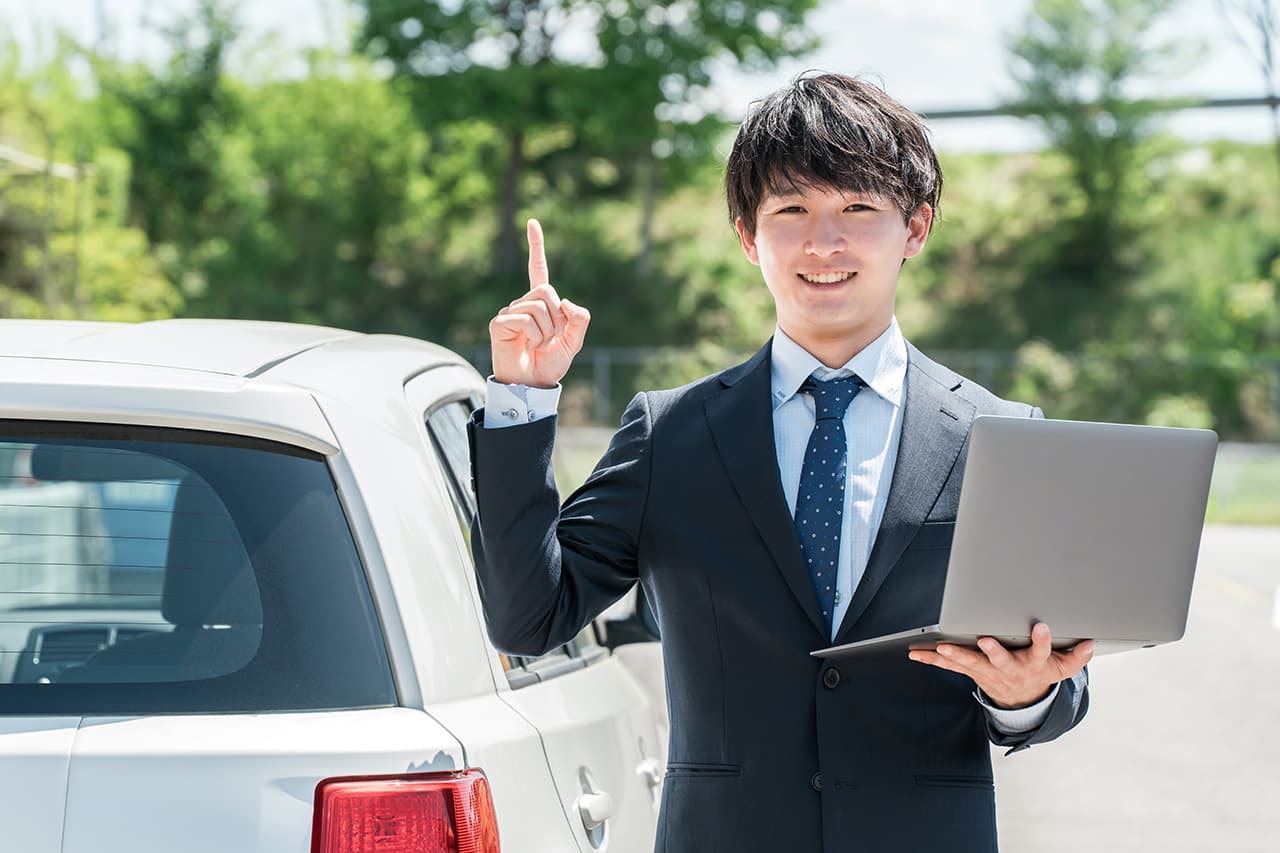 車の横でPCを片手に笑顔の男性